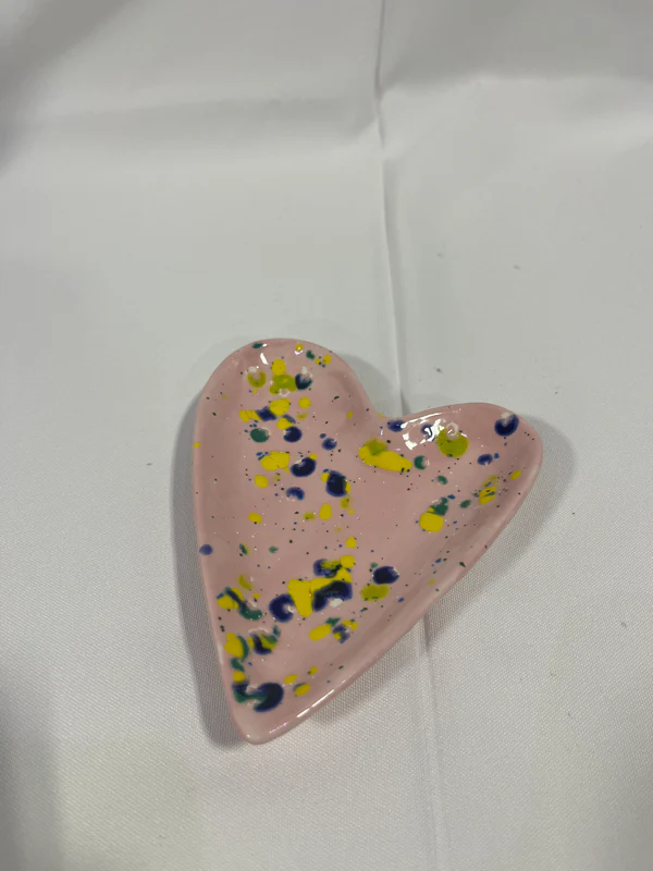 The Heart Jewelry Dish is a pink dish with yellow, blue, and green dots on it.