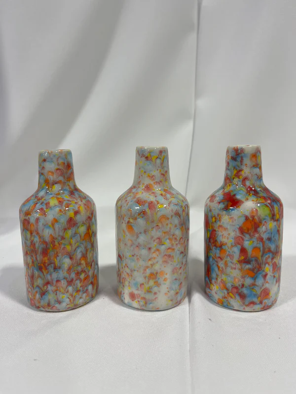 The Jug Bud vases are resting on a table. They are a translucent white with green, red, orange, and blue patterns.