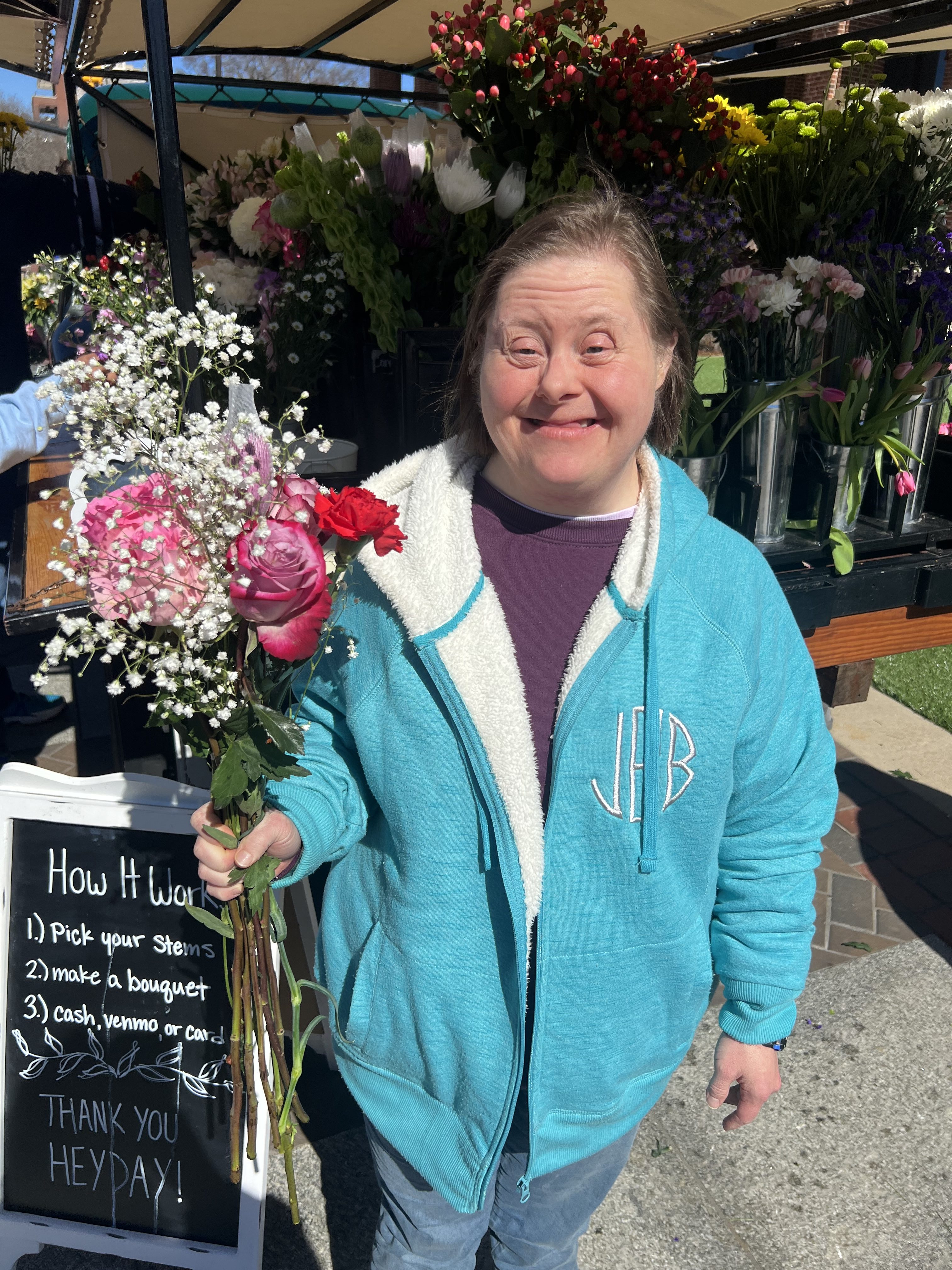 A woman in a blue jacket smiles and holds a bouquet of flowers.