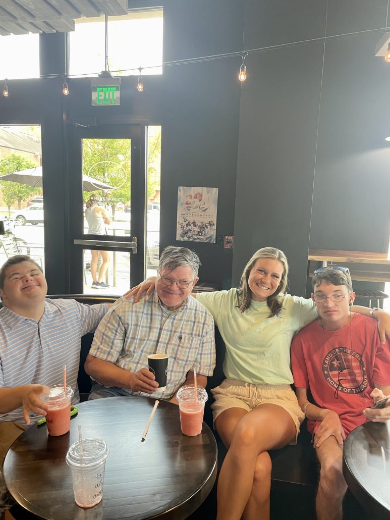 Three men and a woman smile while sitting on a couch at a coffee shop.