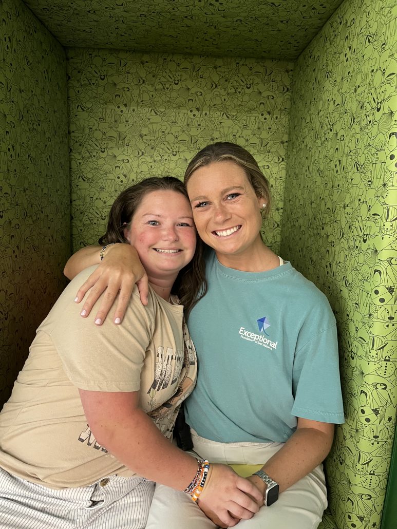 Two women sitting on a green chair smile, hug, and hold hands.