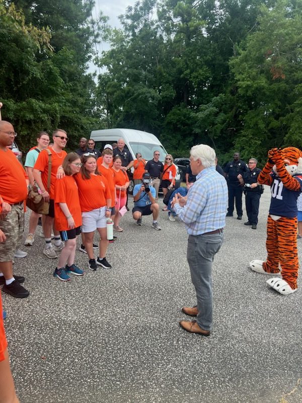 A man in a blue shirt talks to a group of people in orange shirts.
