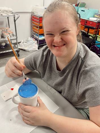 Smiling woman with paintbrush and blue paint.